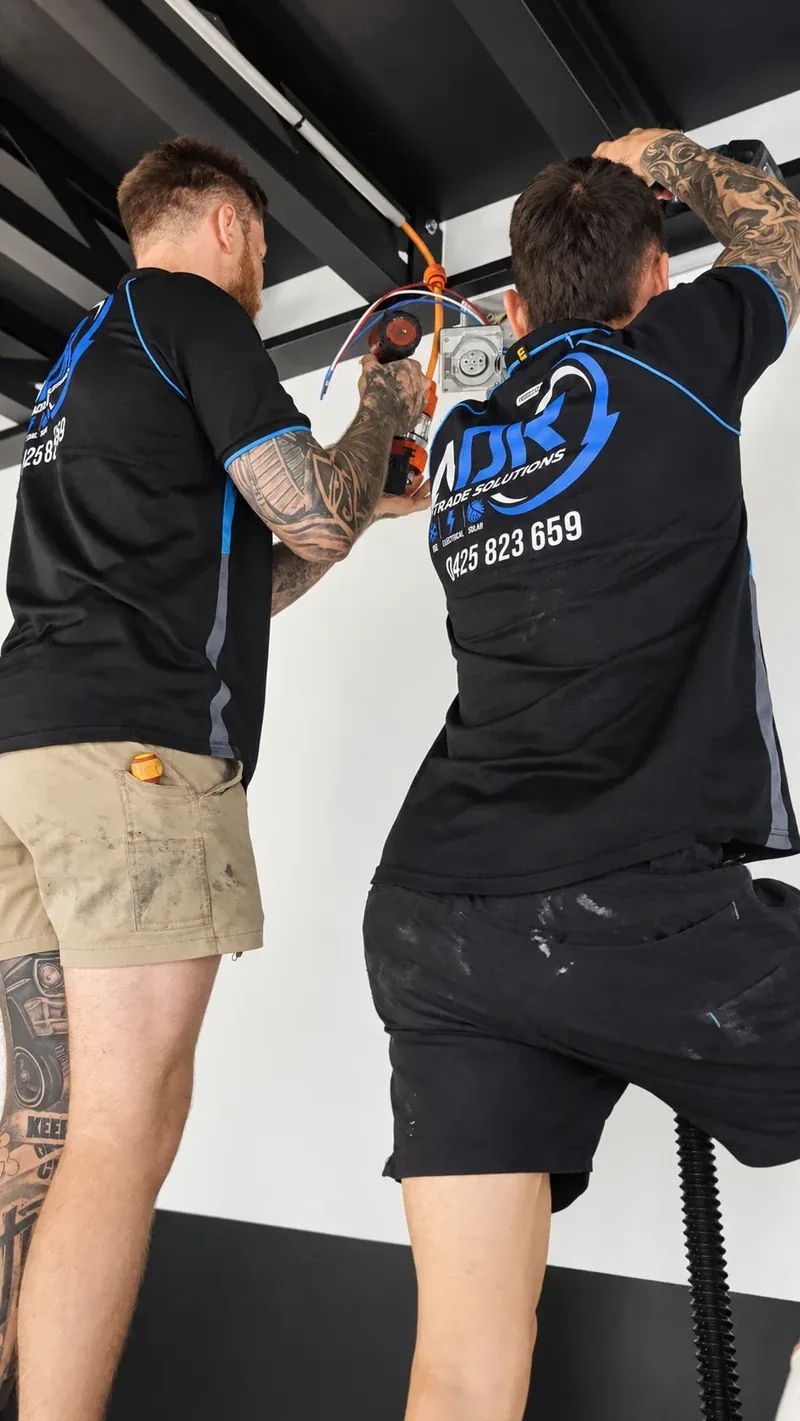 Two NDR electricians working on wiring and a wall-mounted electrical fitting