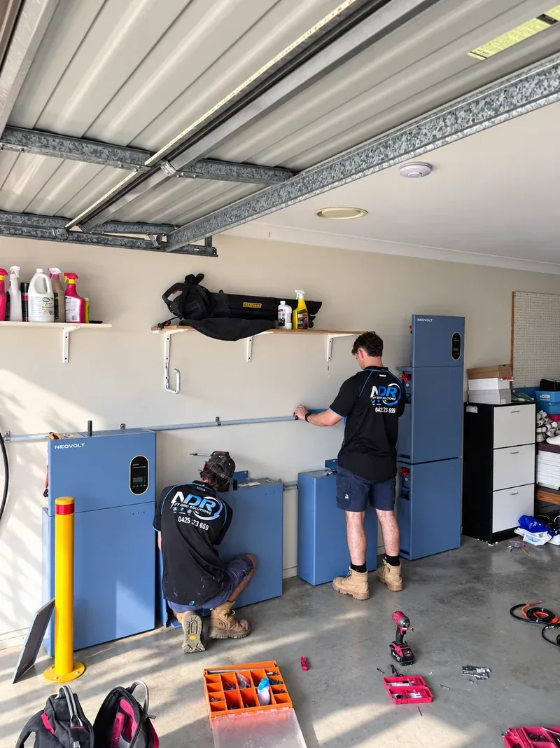 Two NDR technicians installing home battery storage in a garage